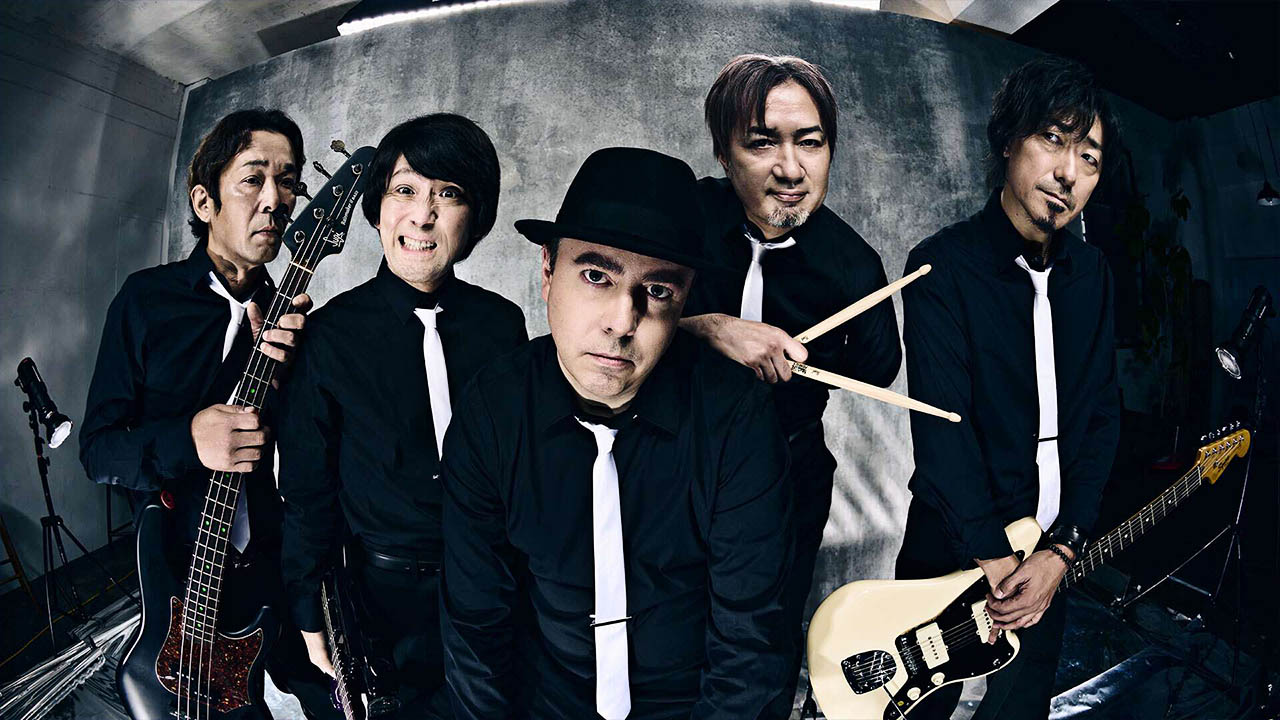 The Primals band members wearing matching black dress shirts and white ties looking into the camera.